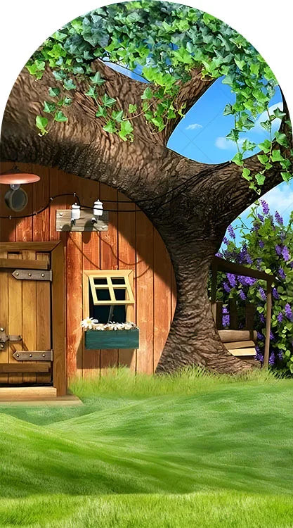 A large tree trunk with green leaves frames a wooden building and a grassy lawn for a birthday party backdrop.