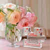 A clear glass vase filled with pink and peach roses next to a personalized acrylic block puzzle engraved with I love you for 
