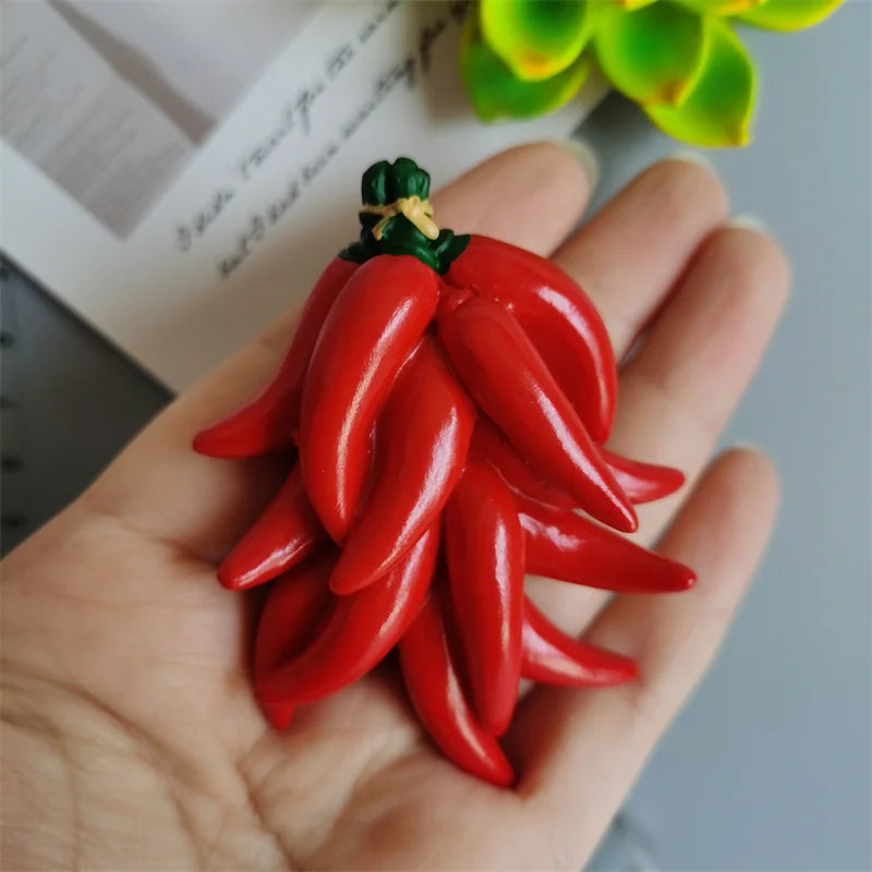 A hand holds a set of playful food-shaped fridge magnets, resembling red chili peppers.