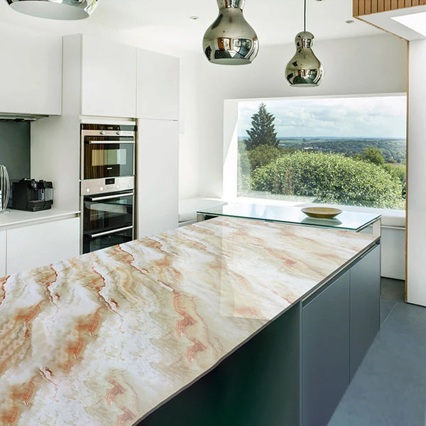 A kitchen countertop made of marbled pink and beige stone with a dark green base, featuring modern cabinetry and pendant ligh