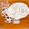 A set of white 3D Halloween cookie cutters and fondant stamps shaped like pumpkins, ghosts, and bats on a wooden surface.