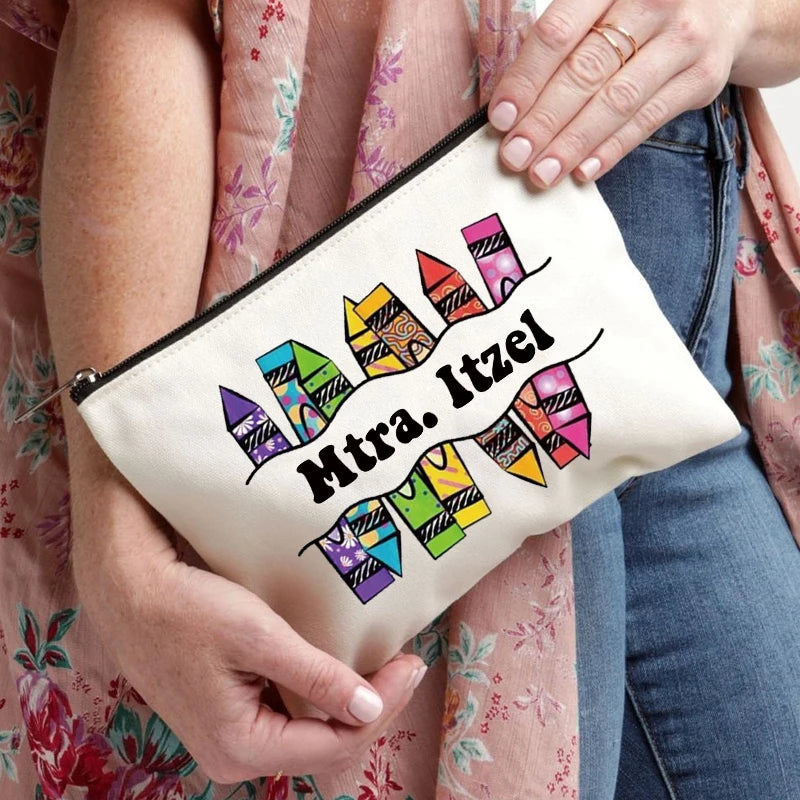 A beige canvas makeup bag with colorful geometric designs and the name Mtra. Itzel is held by a person wearing a pink floral 