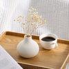 Three minimalist white ceramic decorative vases displayed on a wooden tray with dried floral branches and a cup of black coff