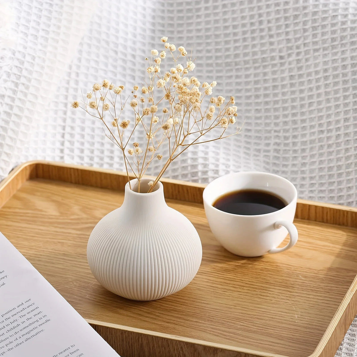 Three minimalist white ceramic decorative vases displayed on a wooden tray with dried floral branches and a cup of black coff