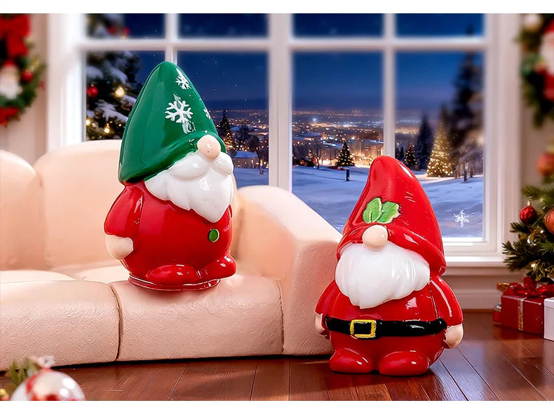 A festive resin Christmas dwarf figurine set featuring a green and white gnome on a pink sofa near a snowy window view.