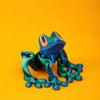 A vibrant teal tree frog ornament with large eyes is displayed against a solid orange background.