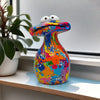 A colorful resin figurine shaped like a frog with large eyes sitting on a shelf next to a houseplant.