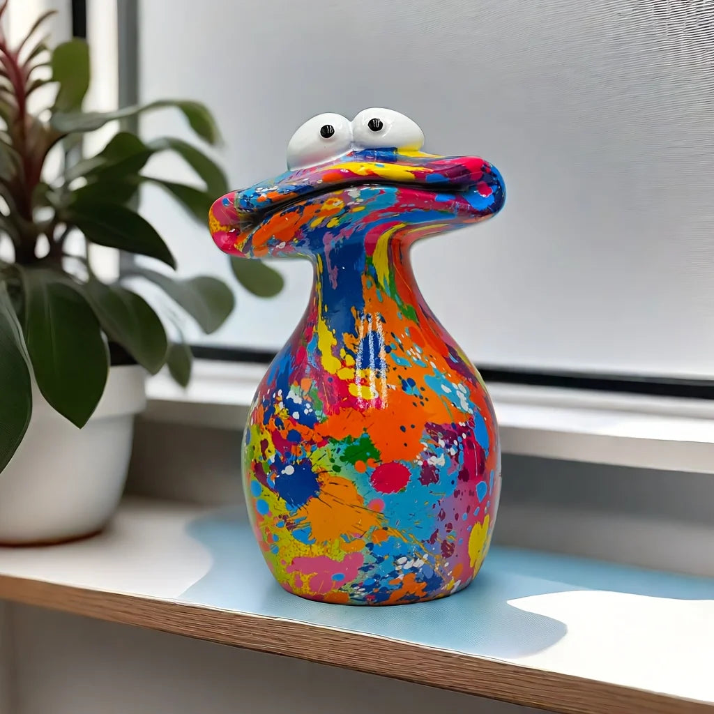 A colorful resin figurine shaped like a frog with large eyes sitting on a shelf next to a houseplant.