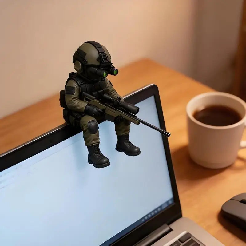 A tactical sniper soldier figurine in olive green gear is displayed on a laptop screen next to a cup of coffee.