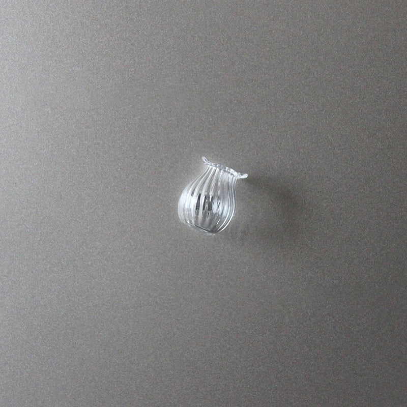 A clear glass fridge magnet shaped like a small, stylized bell or vase is displayed against a gray background.