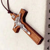 A wooden cross necklace featuring a silver crucifix and a wax rope cord, displayed against a white fabric background.