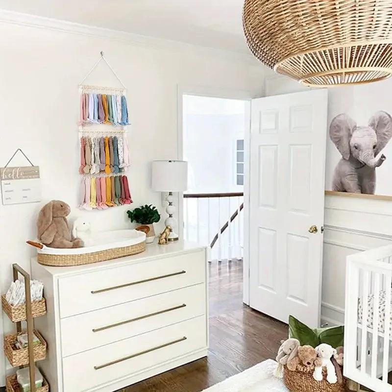 A white dresser with drawers and a wooden tray holds various accessories, including a wall-mounted headband holder for girls.