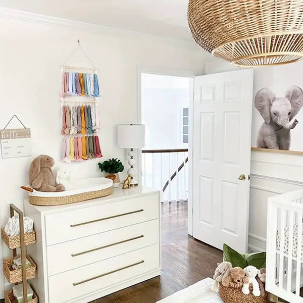 A white dresser with drawers and a wooden tray holds various accessories, including a wall-mounted headband holder for girls.