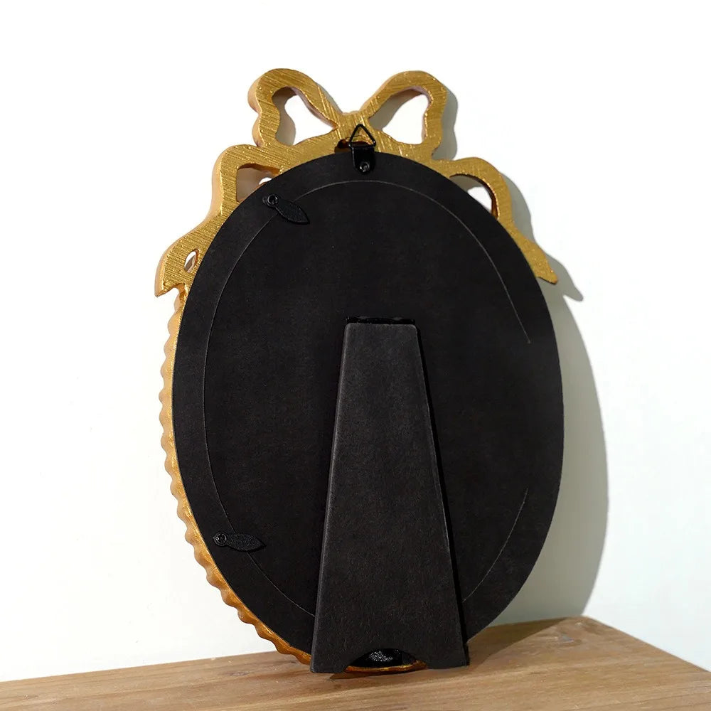 A vintage bowknot picture frame in black with gold accents, displayed on a wooden surface.
