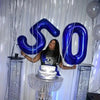 A large dark blue foil number balloon shaped like 50 is suspended in front of a tiered cake decoration.