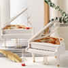 A white hand-crank music box with a ballerina figure and a golden leaf on a white surface.