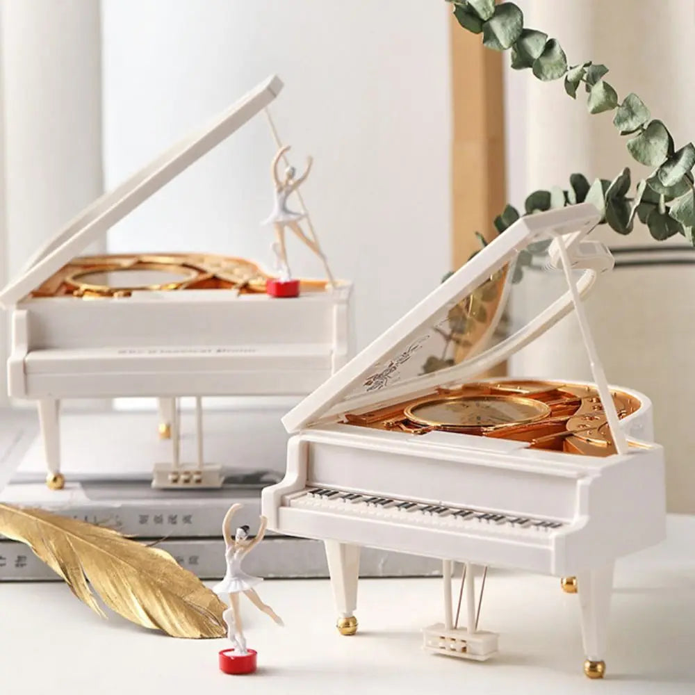 A white hand-crank music box with a ballerina figure and a golden leaf on a white surface.