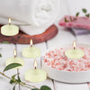 A set of ivory soy wax floating candles in a white bowl surrounded by green leaves and a rolled white towel.