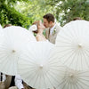 A couple is photographed outdoors surrounded by white oil paper umbrellas for a wedding or decor theme.