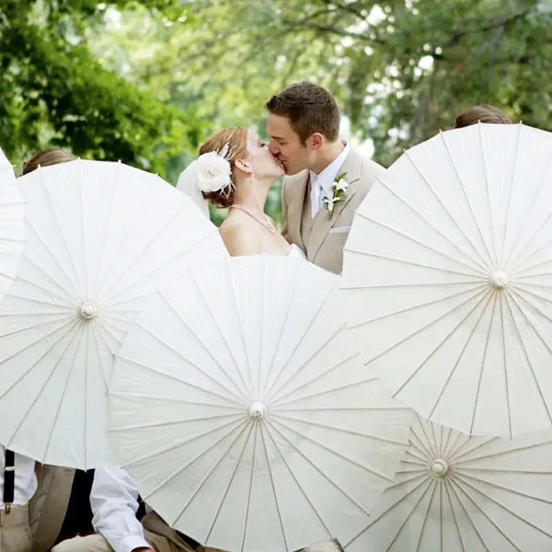 A couple is photographed outdoors surrounded by white oil paper umbrellas for a wedding or decor theme.