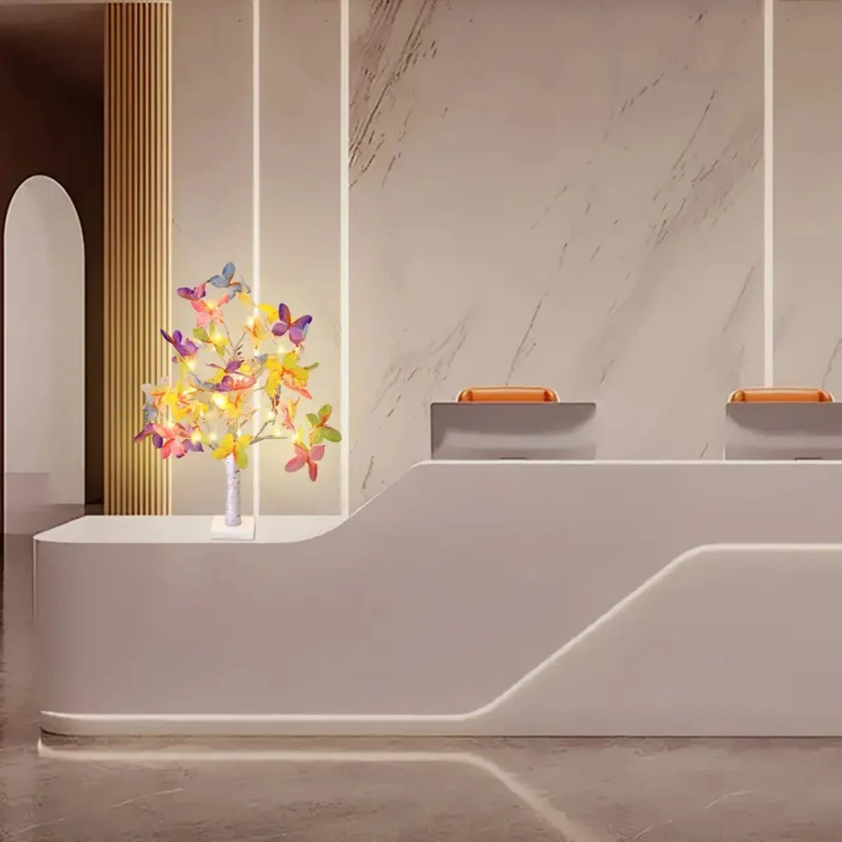 A white modern display featuring a 24-LED butterfly birch tree light with warm glow against a marble wall.