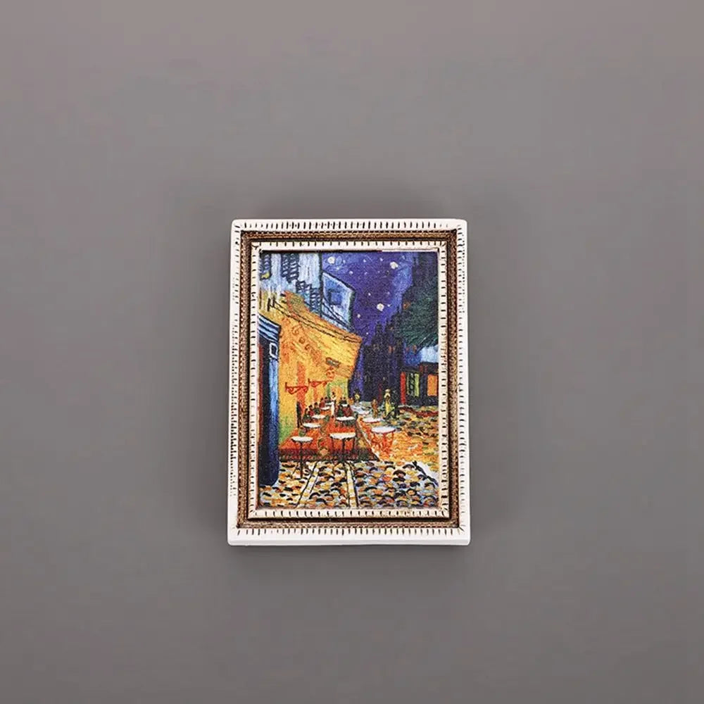 A framed painting featuring a night cityscape with warm yellow lighting and dark blue sky, used as a fridge magnet.