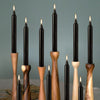 A collection of twelve black taper candles in various wood and black finishes arranged vertically against a muted gray backgr