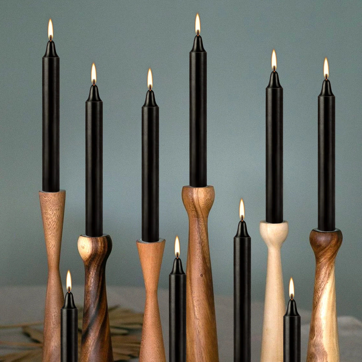A collection of twelve black taper candles in various wood and black finishes arranged vertically against a muted gray backgr