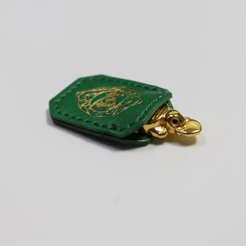 A small, olive green leather pouch with a gold embossed tortoise design and a brass figurine attached.