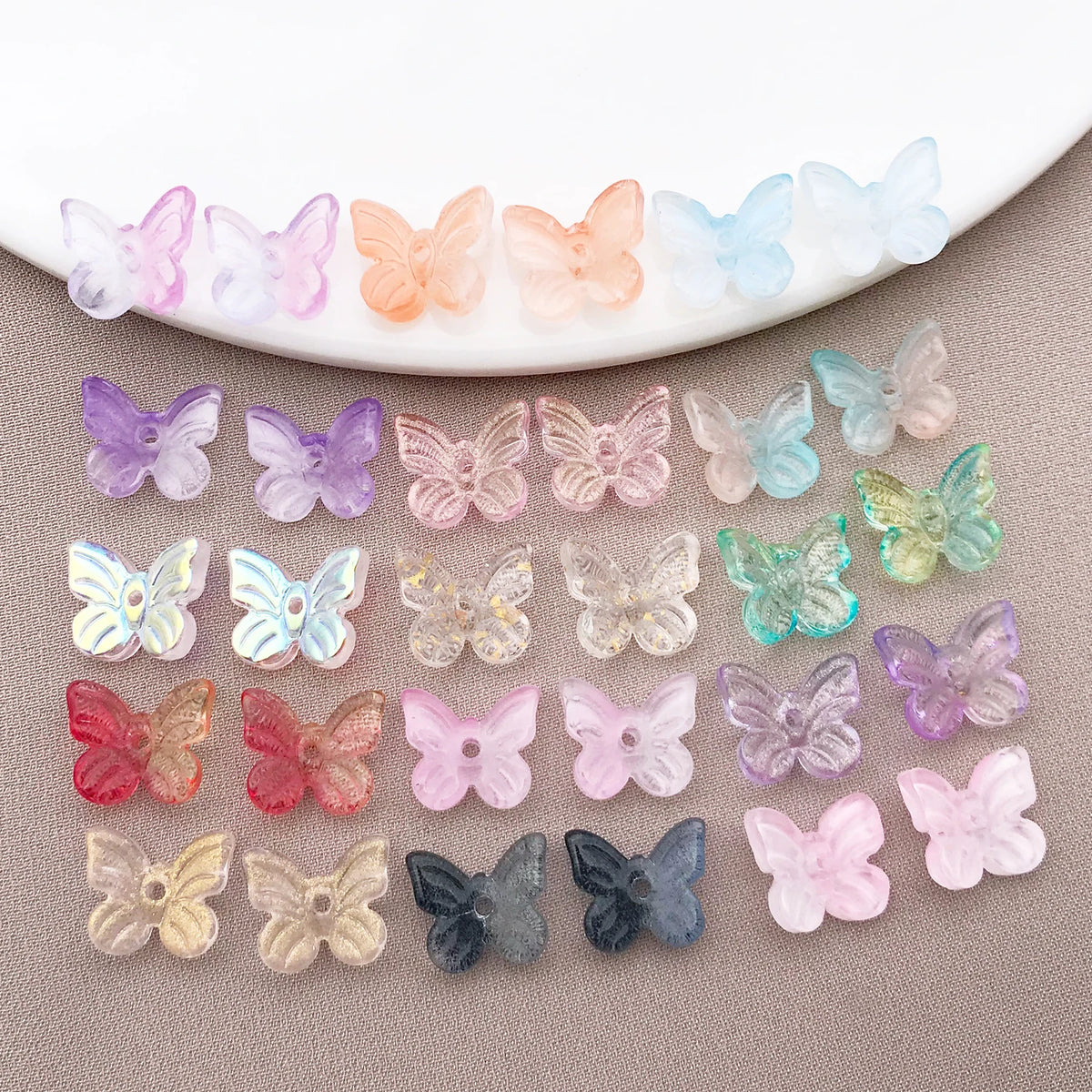 Variedad de cuentas de mariposa de vidrio de colores dispuestas en un plato blanco.