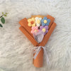 A bouquet of handcrafted crochet sunflowers in yellow, white, and blue flowers wrapped in orange paper on a white fluffy surf