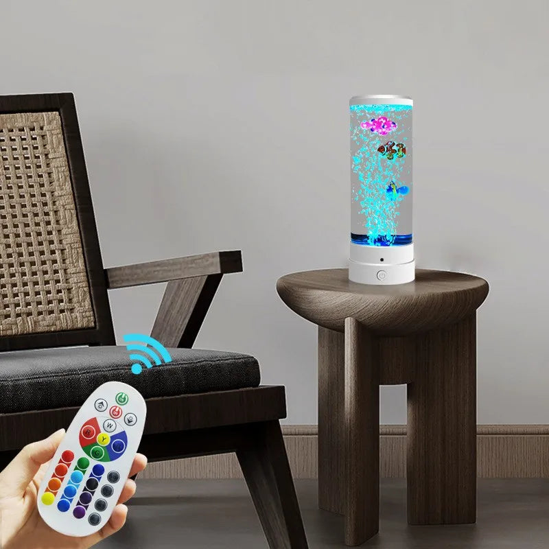 A color-changing LED fish lamp is displayed on a wooden table next to a person holding a remote control.