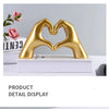 Gold heart-shaped resin hand sculpture displayed on a white book for detail view.