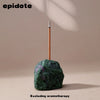 A dark green stone with purple inclusions is shown with a thin stick, likely an incense holder.