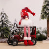 A red and white knitted gnome decoration with a white beard and red hat sits on an antique wooden cart in a snowy outdoor set