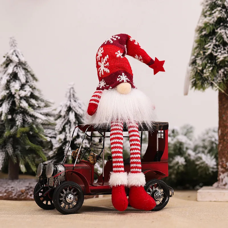 A red and white knitted gnome decoration with a white beard and red hat sits on an antique wooden cart in a snowy outdoor set