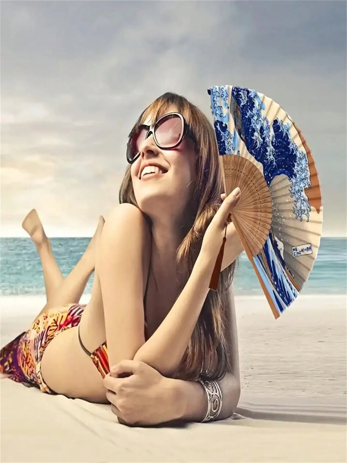 A woman smiling while holding a Japanese foldable hand fan with a Kanagawa wave design on a beach.