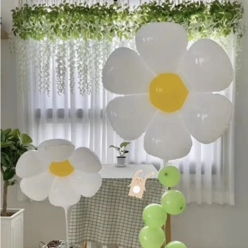 A cluster of white and yellow foil balloons resembling daisies hangs in front of a sheer curtain.