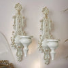 A pair of vintage white wrought iron wall-mounted candle holders with ornate detailing.