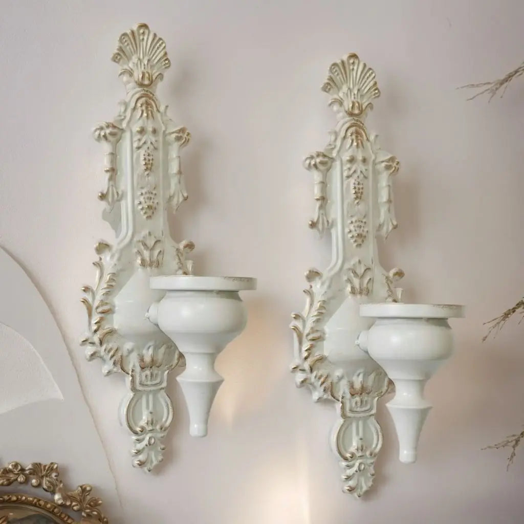 A pair of vintage white wrought iron wall-mounted candle holders with ornate detailing.