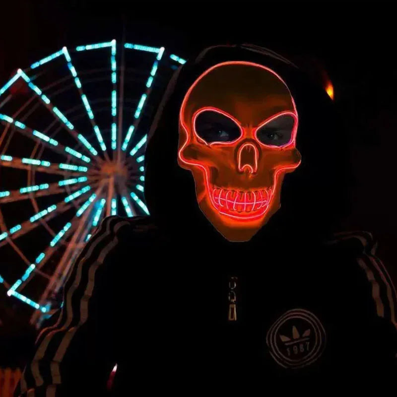A person wearing a glowing orange skull mask in a dark setting with blue light effects visible behind them.
