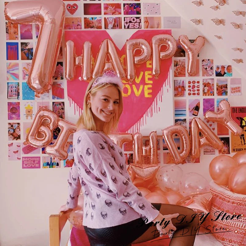 A young woman smiling in front of a pink and gold balloon decoration featuring large foil letters spelling 'HAPPY BIRTHDAY'