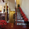 A staircase decorated with bright red artificial poinsettia flowers on the banister and steps.