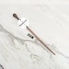 A wooden magic wand replica with a metal core is displayed on a white marble surface.