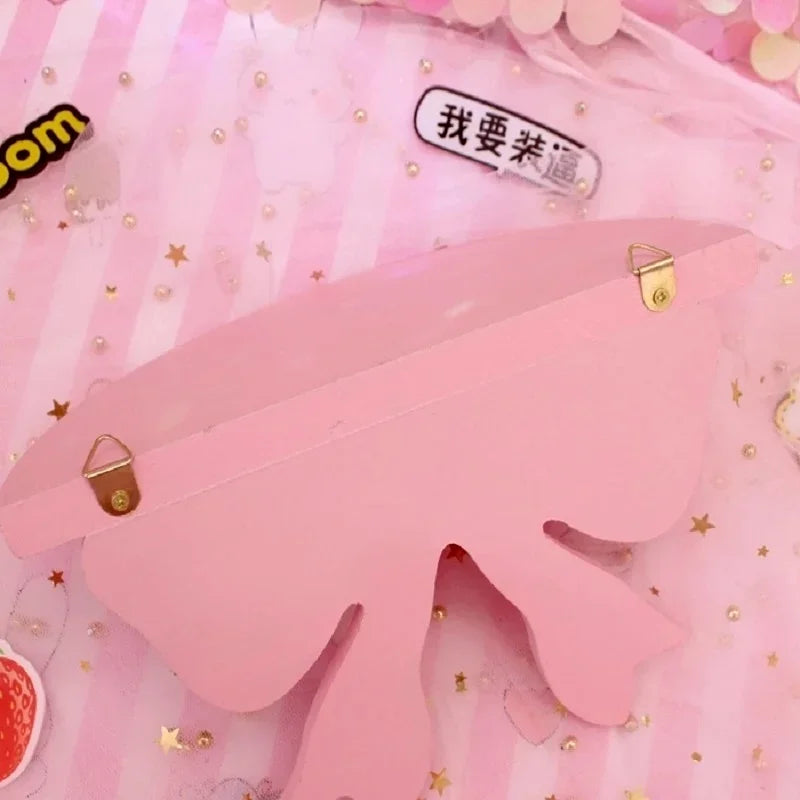 Pink decorative bow-shaped wooden wall shelf with gold hardware set against a pink striped background.
