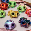 A collection of six 3D printed frog car ornaments with color-shifting eyes in various shades of green, yellow, and pink.