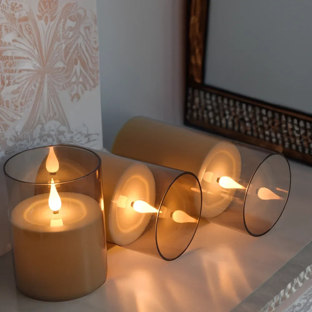 A set of remote control flameless LED candles in a glass holder and cylindrical containers, illuminated with warm light.