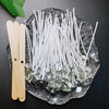 A collection of white cotton candle wicks is displayed on a clear glass plate next to wooden clothespins.