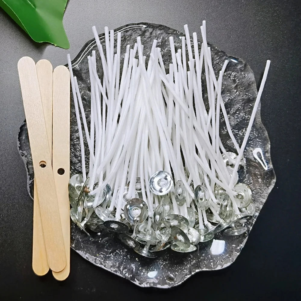 A collection of white cotton candle wicks is displayed on a clear glass plate next to wooden clothespins.
