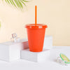 An orange plastic cold cup with a lid and straw is displayed on a white surface next to ice cubes.